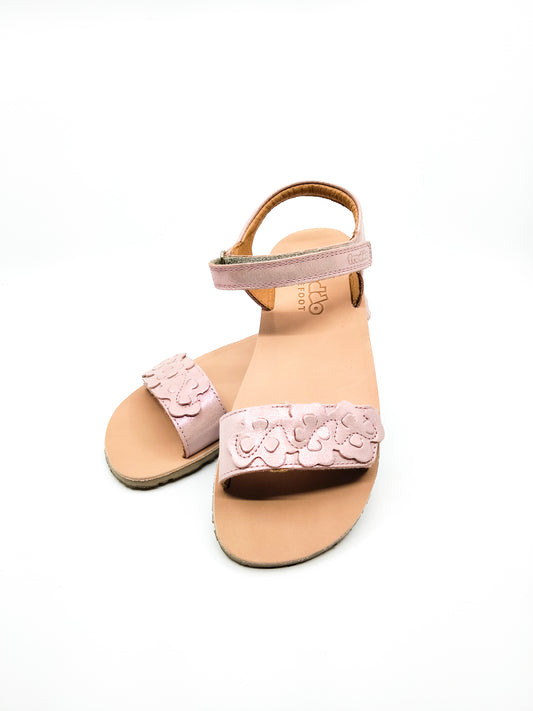 Kauniit pinkin hohtavat sandaalit, missä nahkaan leikattu jalkapöydän päälle kukkakuvioita
